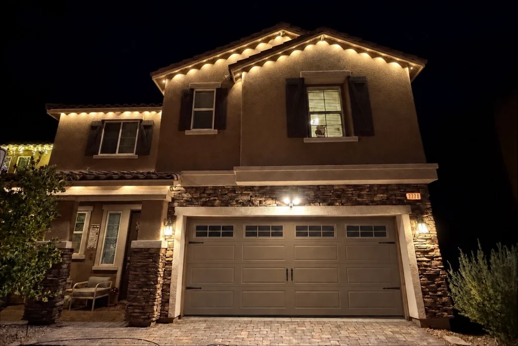 Warm-white permanent roofline lights illuminating a home's exterior at night.